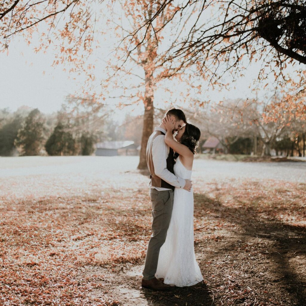 Bride and groom getting ready to kiss in a field with a tree behind them