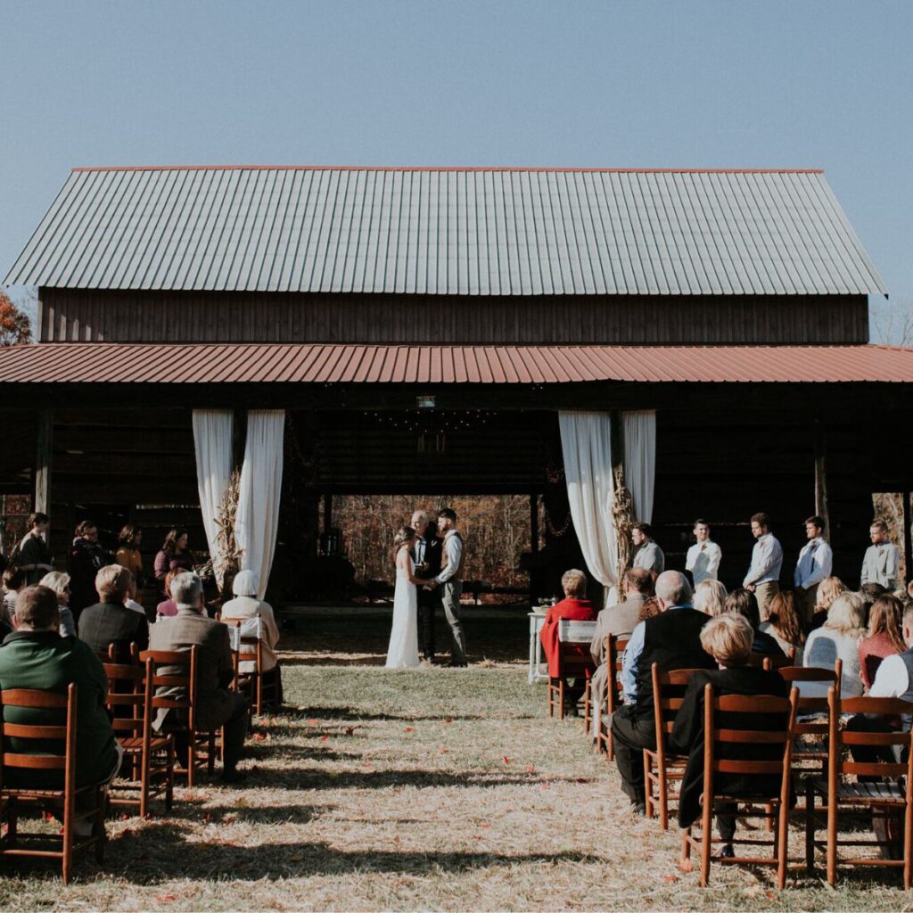 a photo of a couple getting married at a barn with all of the guests seated around them