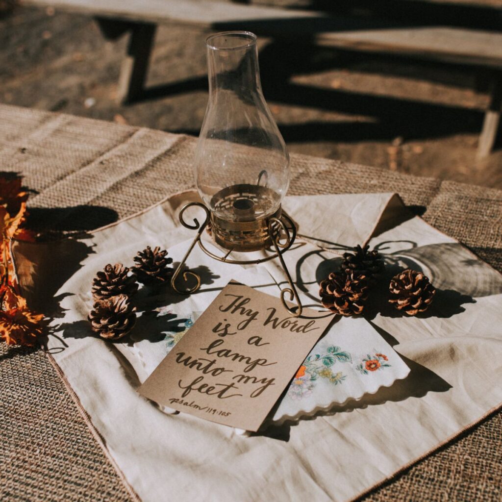 a vintage lamp, a piece of paper with a scripture written on it, a vintage napkin and some pinecones