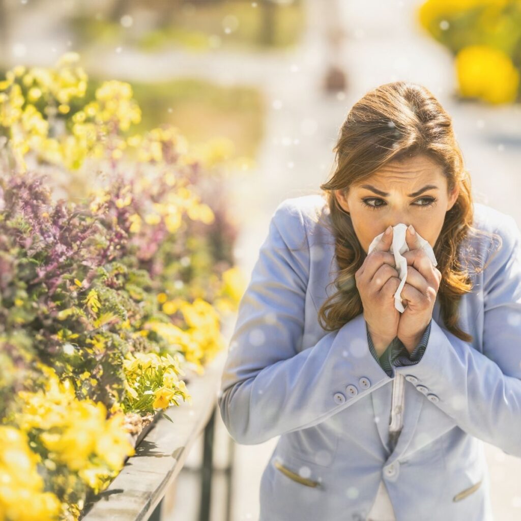 woman standing beside flower holding a tissue over her nose