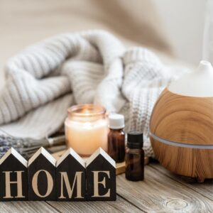 cozy blanket, candle, essential oils, a diffuser and a sign with the word home on it all sitting on a table