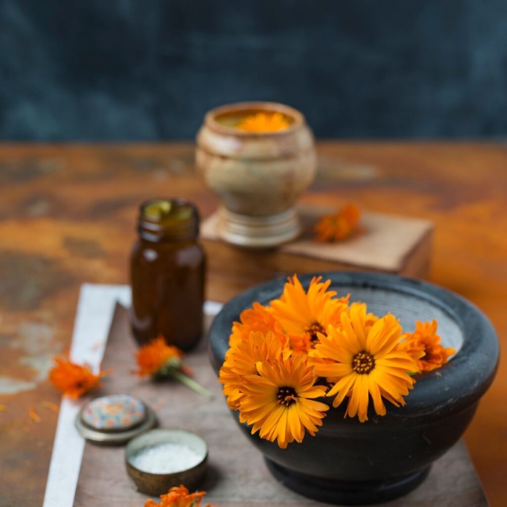 calendula flowers in a bowl with small bottles and lotions beside them.