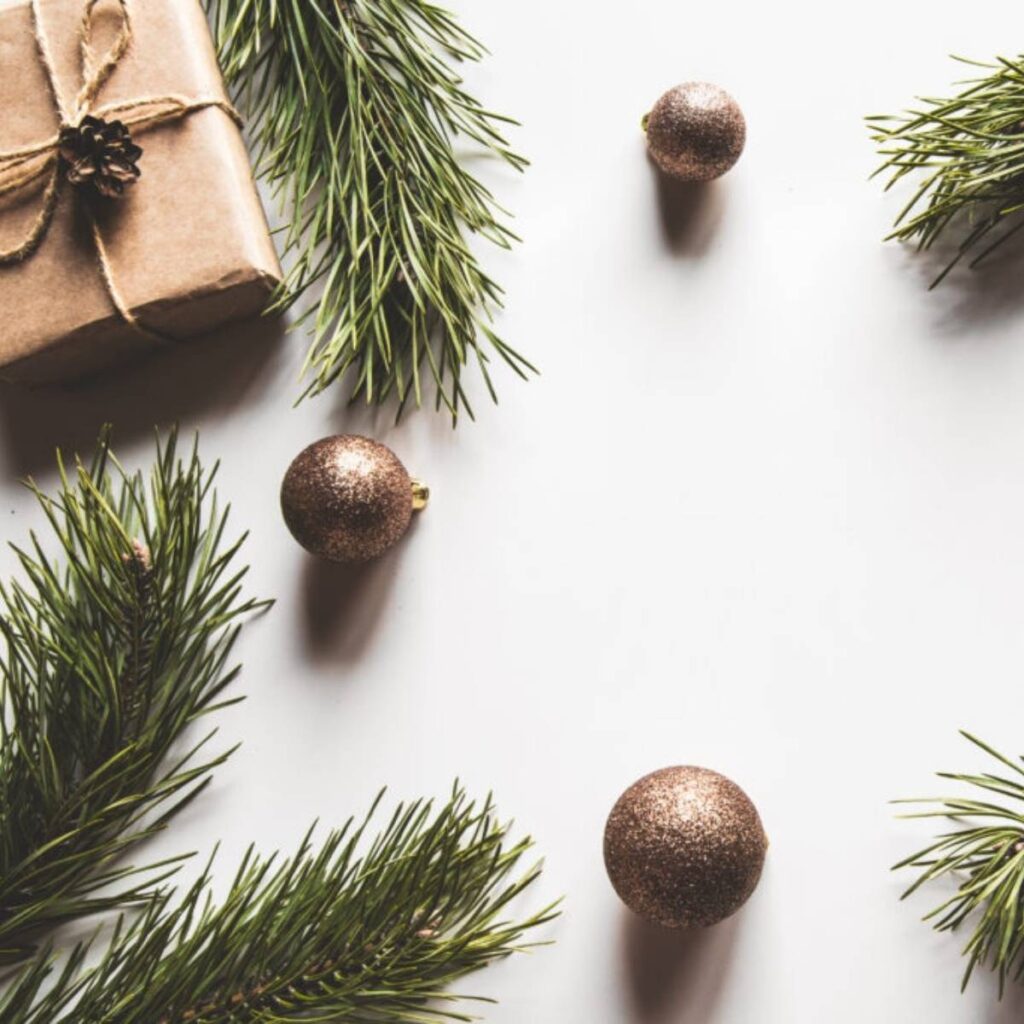 Christmas decorations on white background including gold ornaments, branches and brown paper wrapped gifts