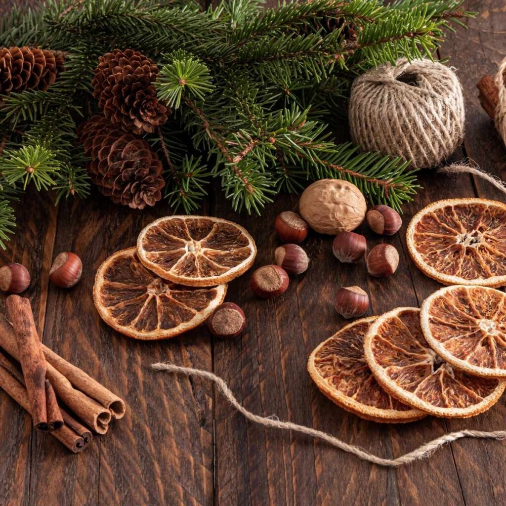 natural Christmas decorations of dried oranges, tree branches, twine, cinnamon sticks, nuts and pinecones on a wooden table. 