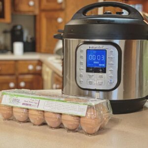 Instant pot sitting on kitchen counter with a dozen cage free brown eggs sitting in front of it in carton