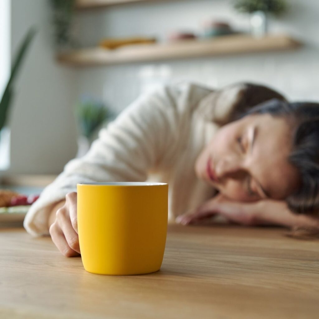 woman laying head on arm on table with a coffee mug in the other hand