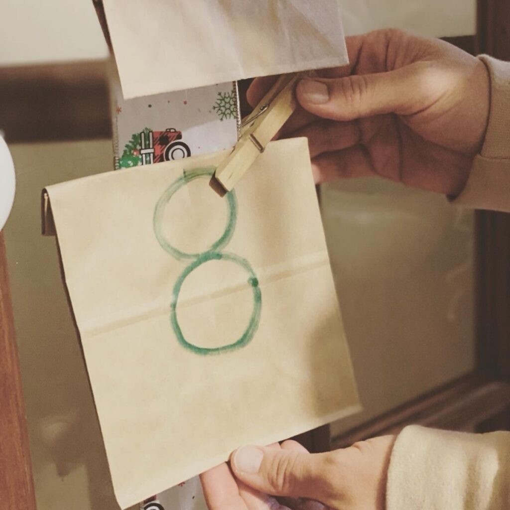 Picture of hands holding a paper bag with the number eight written on it using a clothespin to hold it to ribbon