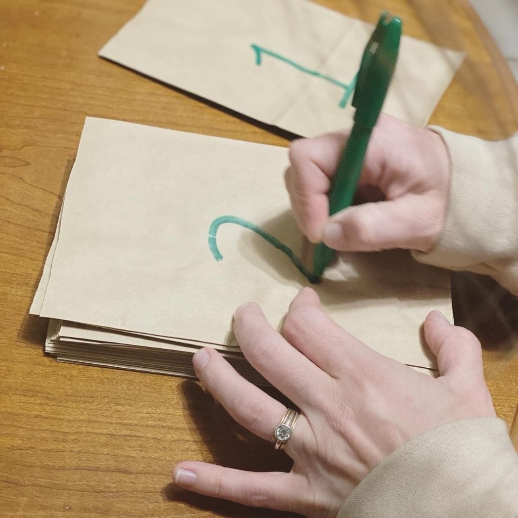 picture of hands holding a green marker writing the numbers one and two on a paper bags