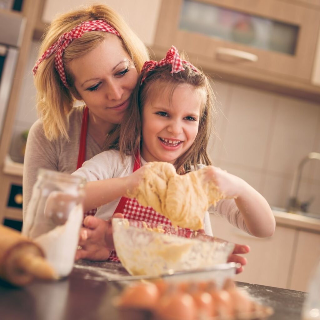mom with her daughter in the kitchen teaching her how to cook