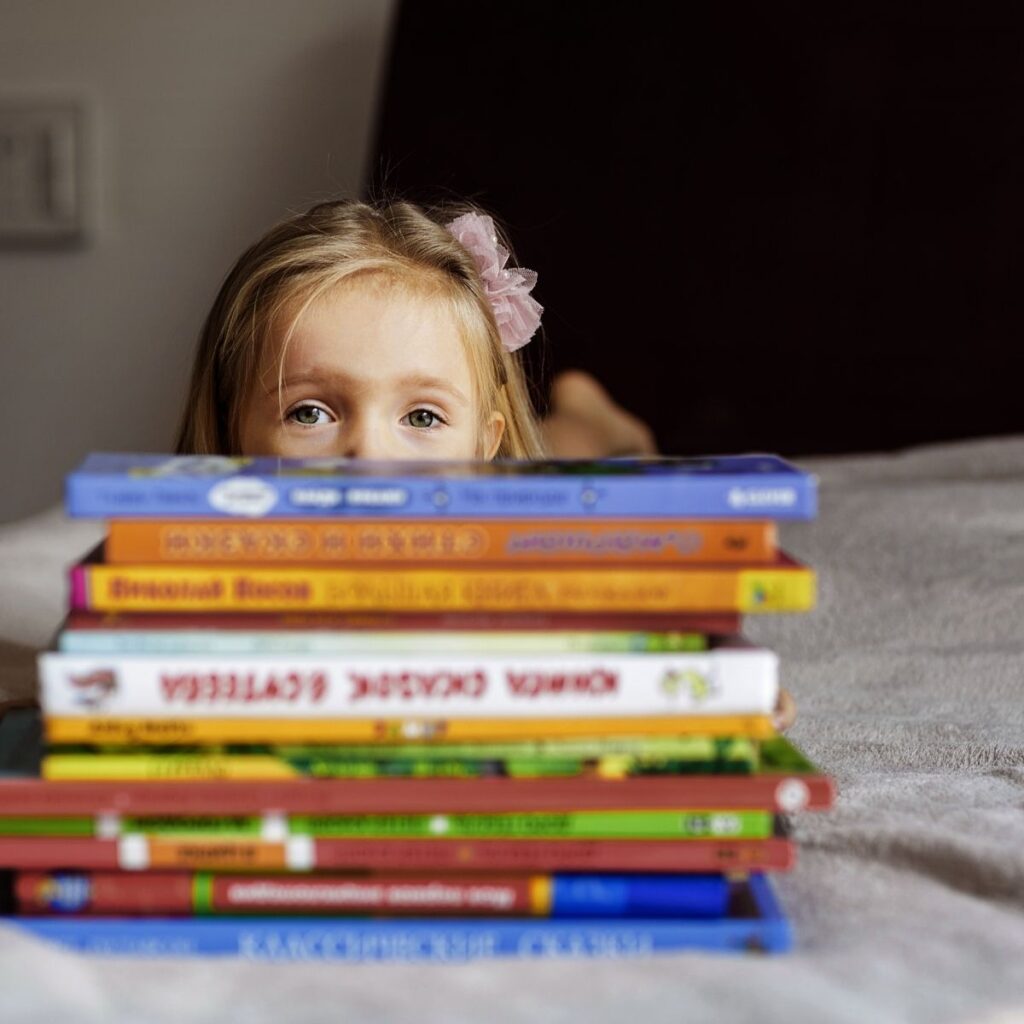 little girl laying on bed with a stack of children's books in front of her