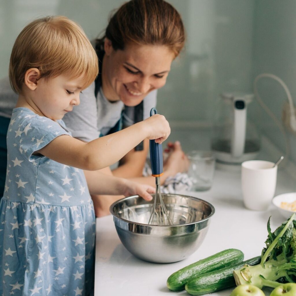 toddler cooking with her mom in the kitchen, stirring ingredients in a bowl