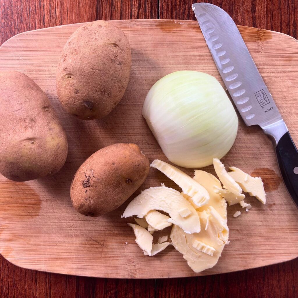 potatoes, butter, an onion and a knife laying on a chopping board
