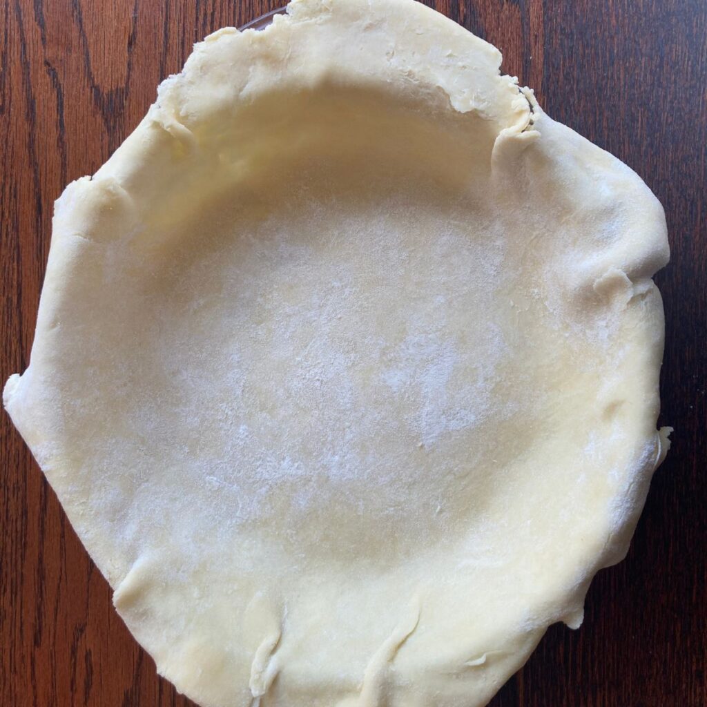 top down photo of a rolled out pie crust in a pie plate with excess hanging over the sides